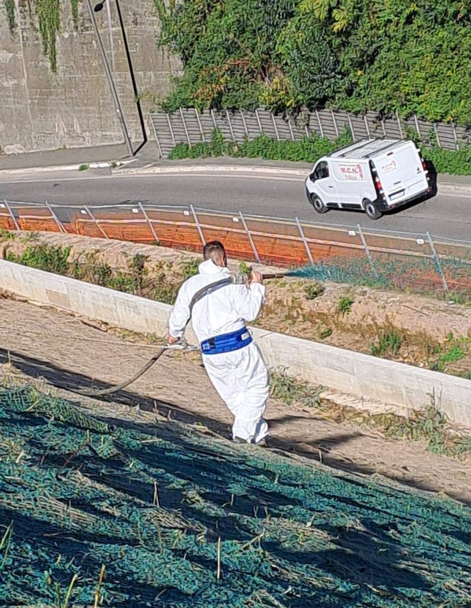 Operatore che idrosemina a mano una scarpata lungo la strada